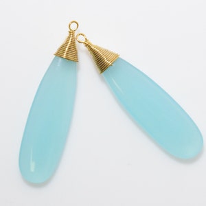 May include: Two light blue teardrop-shaped gemstone pendants with gold wire wrapped around the top of each pendant.