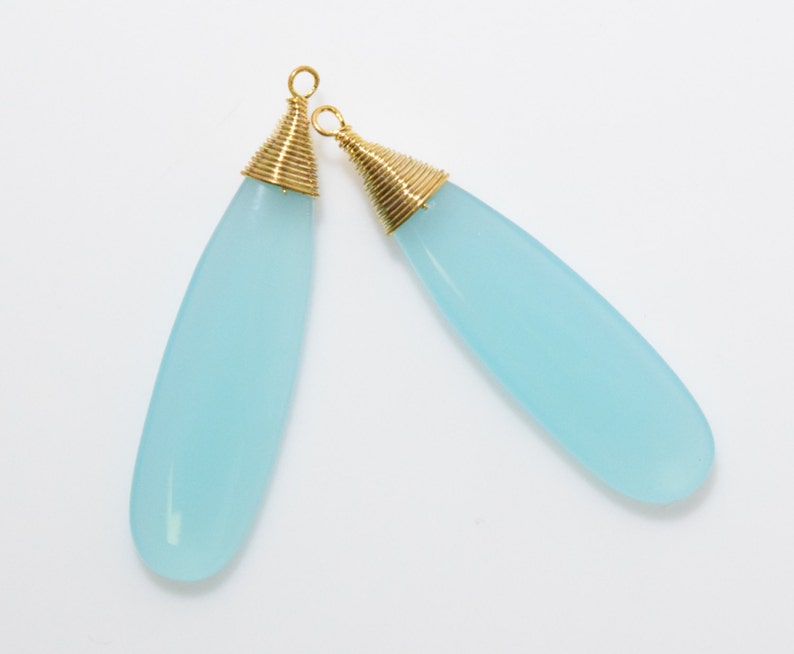 May include: Two light blue teardrop-shaped gemstone pendants with gold wire wrapped around the top of each pendant.