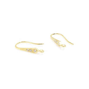 May include: A pair of gold-tone earring hooks with clear crystal accents. The hooks are designed with a pointed end and a small loop at the top.