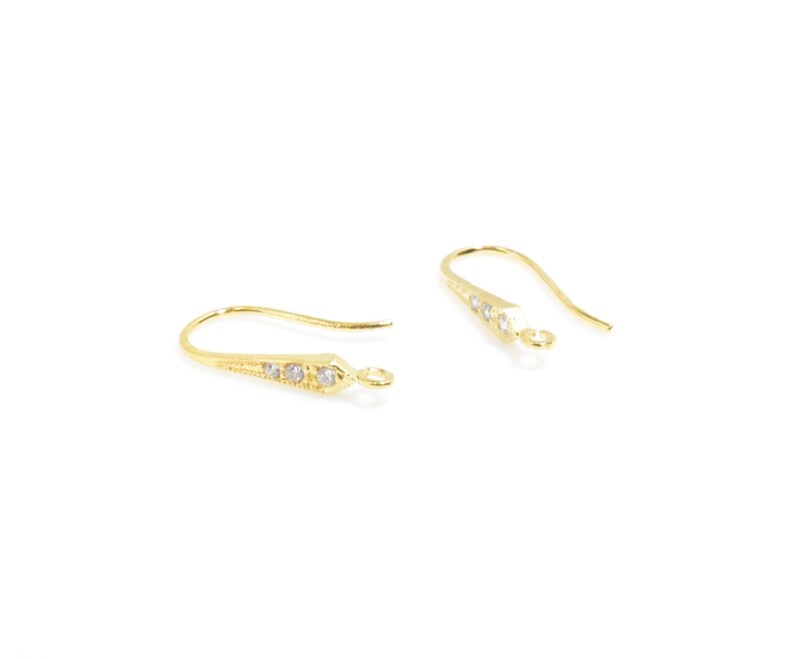 May include: A pair of gold-tone earring hooks with clear crystal accents. The hooks are designed with a pointed end and a small loop at the top.