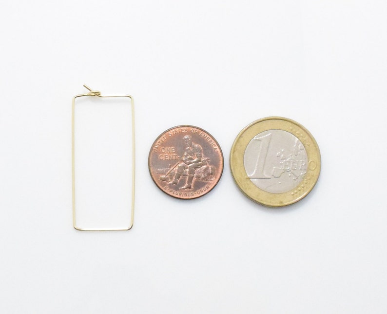 May include: Gold rectangle hoop earrings, shown next to a US penny and a Euro coin for size comparison.