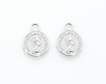 May include: Two silver charm pendants with a detailed design of a woman's profile with a crown and text around the edge.