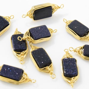 May include: Several rectangular blue sandstone beads with gold wire wrapping. The beads have a speckled appearance and are encased in intricate gold wire designs, with loops at each end for stringing. The gold wire adds a decorative element to the beads.