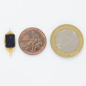 May include: A rectangular, dark blue gemstone pendant with gold wire wrapping, next to a US penny and a Euro coin. The gemstone has a speckled appearance. The pendant is designed with a loop at the top and bottom for attachment.