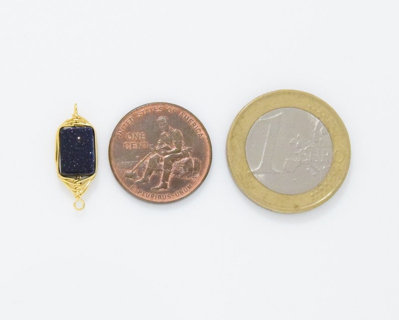 May include: A rectangular, dark blue gemstone pendant with gold wire wrapping, next to a US penny and a Euro coin. The gemstone has a speckled appearance. The pendant is designed with a loop at the top and bottom for attachment.
