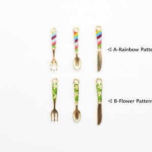May include: Six miniature gold-toned utensils with colorful enamel designs. Two forks, two spoons, and two knives. One set features a rainbow stripe pattern, and the other set features a green floral pattern.