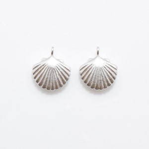 May include: Two silver seashell charms with a detailed, textured design. The charms are perfect for adding a touch of coastal style to jewelry or crafts.