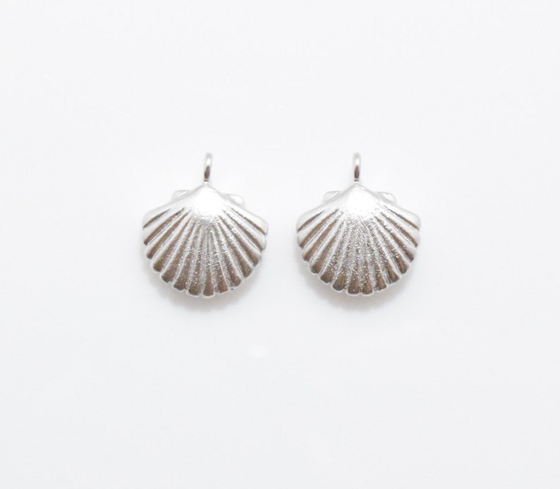 May include: Two silver seashell charms with a detailed, textured design. The charms are perfect for adding a touch of coastal style to jewelry or crafts.