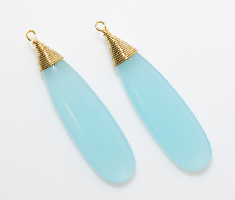 May include: A pair of light blue teardrop-shaped earrings with gold wire wrapped around the top of each earring.
