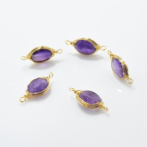K&ouml;nnte beinhalten: F&uuml;nf Amethyst-Edelsteinkugeln, die mit goldfarbenem Draht umwickelt sind und an beiden Enden Schlaufen haben. Die Kugeln sind oval geformt und haben einen violetten Farbton.