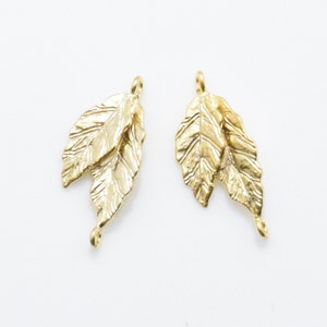 Pode incluir: Dois pingentes de metal dourado em forma de folha com uma superf&iacute;cie texturizada. Cada pingente tem duas folhas e um la&ccedil;o na parte superior para prender em joias.