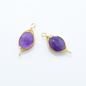 K&ouml;nnte beinhalten: Zwei goldene, drahtgewickelte Anh&auml;nger mit Amethyststeinen. Die Steine sind oval geformt und haben eine violette Farbe.
