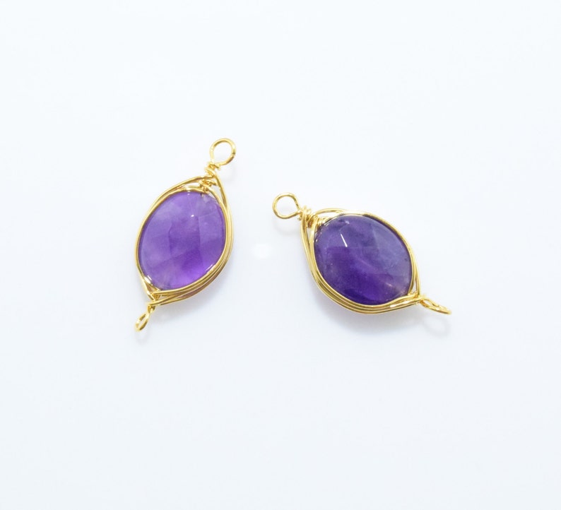 K&ouml;nnte beinhalten: Zwei goldene, drahtgewickelte Anh&auml;nger mit Amethyststeinen. Die Steine sind oval geformt und haben eine violette Farbe.