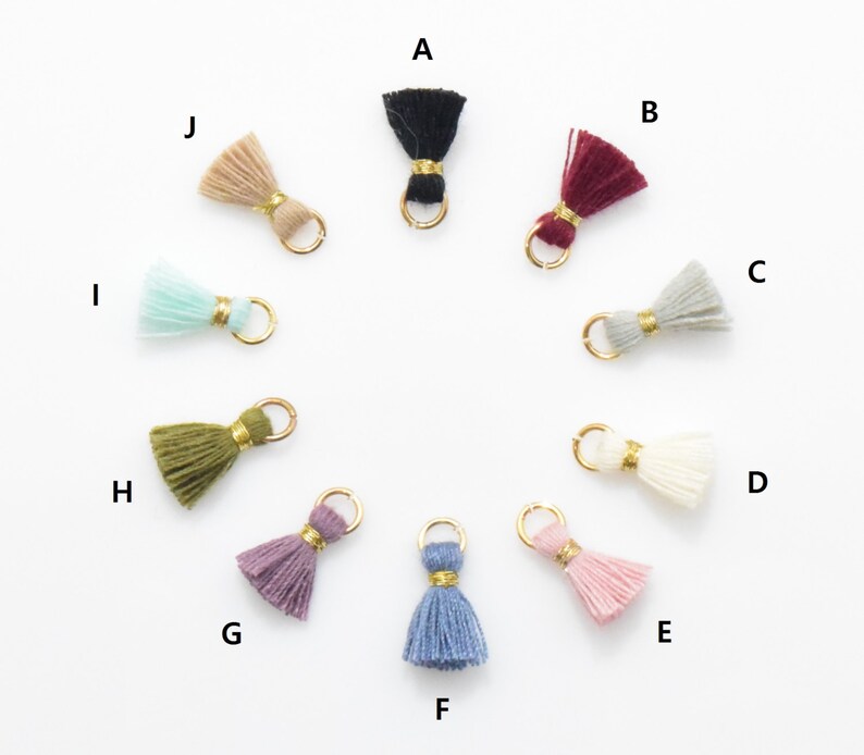 May include: Ten different colored tassel charms with gold jump rings. The tassels are in the colors black, burgundy, gray, white, purple, blue, green, light blue, beige, and pink.