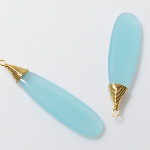 May include: Two light blue chalcedony gemstone pendants with gold wire wrapped around the top of each pendant.