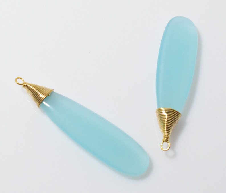 May include: Two light blue chalcedony gemstone pendants with gold wire wrapped around the top of each pendant.