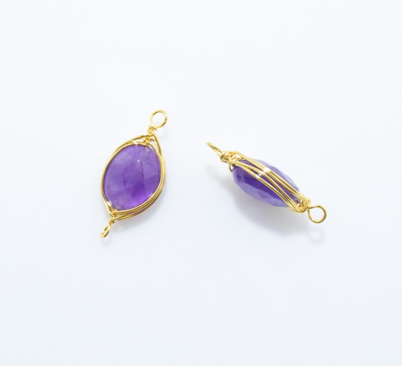 K&ouml;nnte beinhalten: Zwei golddrahtgewickelte Amethyst-Anh&auml;nger. Die Edelsteine sind oval geformt und haben einen violetten Farbton. Der Draht ist um die Edelsteine gewickelt, um ein filigranes und komplexes Design zu schaffen.