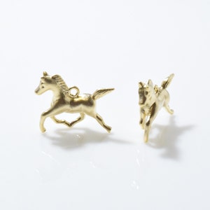 May include: Two gold-colored horse charms, one with its head turned to the left and the other with its head turned to the right.