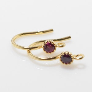 May include: A pair of gold hoop earrings with small, round, dark purple gemstones.
