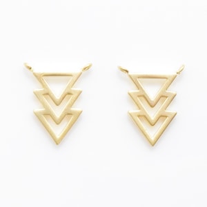 Op de afbeelding: Twee gouden metalen driehoekige hangerbedels met drie gelaagde driehoeken. De bedels hebben een lus aan de bovenkant om aan een ketting of armband te bevestigen.
