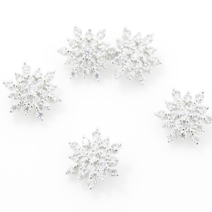 May include: Five silver snowflake-shaped earrings with clear crystal accents.