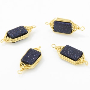 May include: Four gold-colored wire-wrapped pendants. Each pendant features a rectangular, dark blue stone with sparkling inclusions. The wire is intricately woven around the stone, creating a decorative frame with loops at each end.