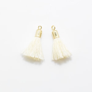 May include: Two white tassel charms with gold metal tops. The tassels are made of soft, fluffy yarn and are perfect for adding a touch of elegance to any project.