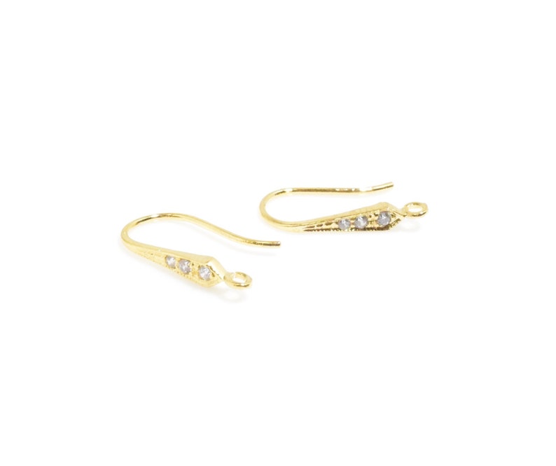 May include: A pair of gold-tone earring hooks with clear crystal accents. The hooks are designed with a pointed end and a small loop at the top.