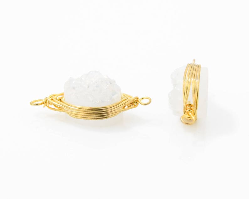 Pu&ograve; includere: Due ciondoli in cristallo bianco avvolti in filo d'oro. I cristalli hanno una forma a grappolo e sono avvolti in filo d'oro. I ciondoli sono su uno sfondo bianco.