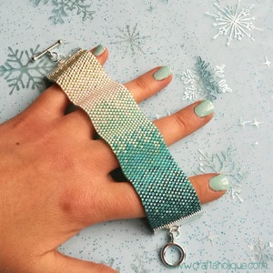 May include: A green and white beaded bracelet with a silver clasp and ring. The bracelet is made with small, square beads that create a gradient effect.