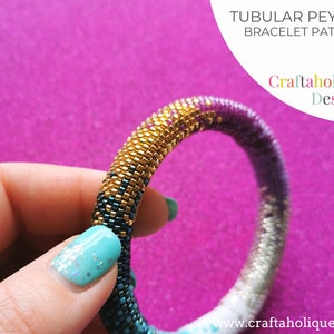 May include: A tubular peyote bracelet pattern with a gradient design, transitioning from gold to teal, purple, and silver. The bracelet is held against a pink background. Text on the image reads "TUBULAR PEYOTE BRACELET PATTERN" and "Craftaholique Designs."