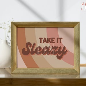 Könnte beinhalten: Goldfarbener gerahmter Druck mit abstraktem Hintergrund in Pfirsich-, Rosa- und Brauntönen. Der Text "Take it Sleazy" ist in Braun mit einer Retro-Schriftart.