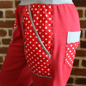 May include: Red and grey women's pants with a white polka dot pocket. The pants have a grey waistband and a grey pocket on the right side.