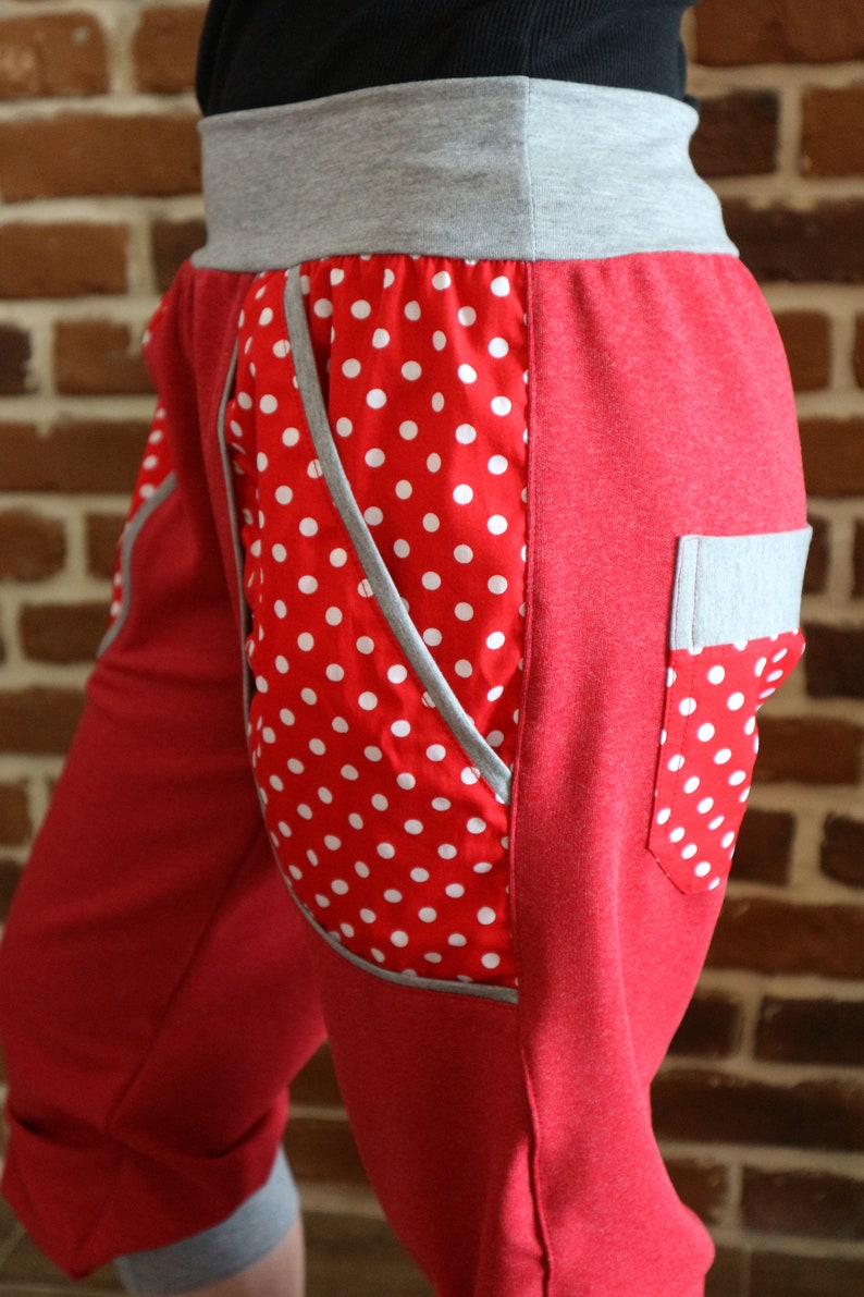 May include: Red and grey women's pants with a white polka dot pocket. The pants have a grey waistband and a grey pocket on the right side.