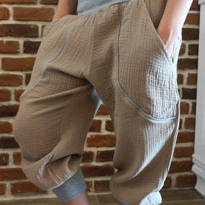 May include: Beige cotton pants with a gray waistband and gray trim. The pants have pockets on the sides and are cuffed at the bottom. The pants are being worn with gray and white sneakers.