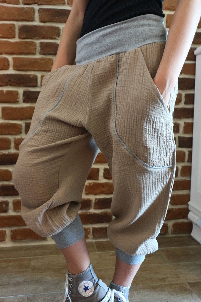 May include: Beige cotton pants with a gray waistband and gray trim. The pants have pockets on the sides and are cuffed at the bottom. The pants are being worn with gray and white sneakers.