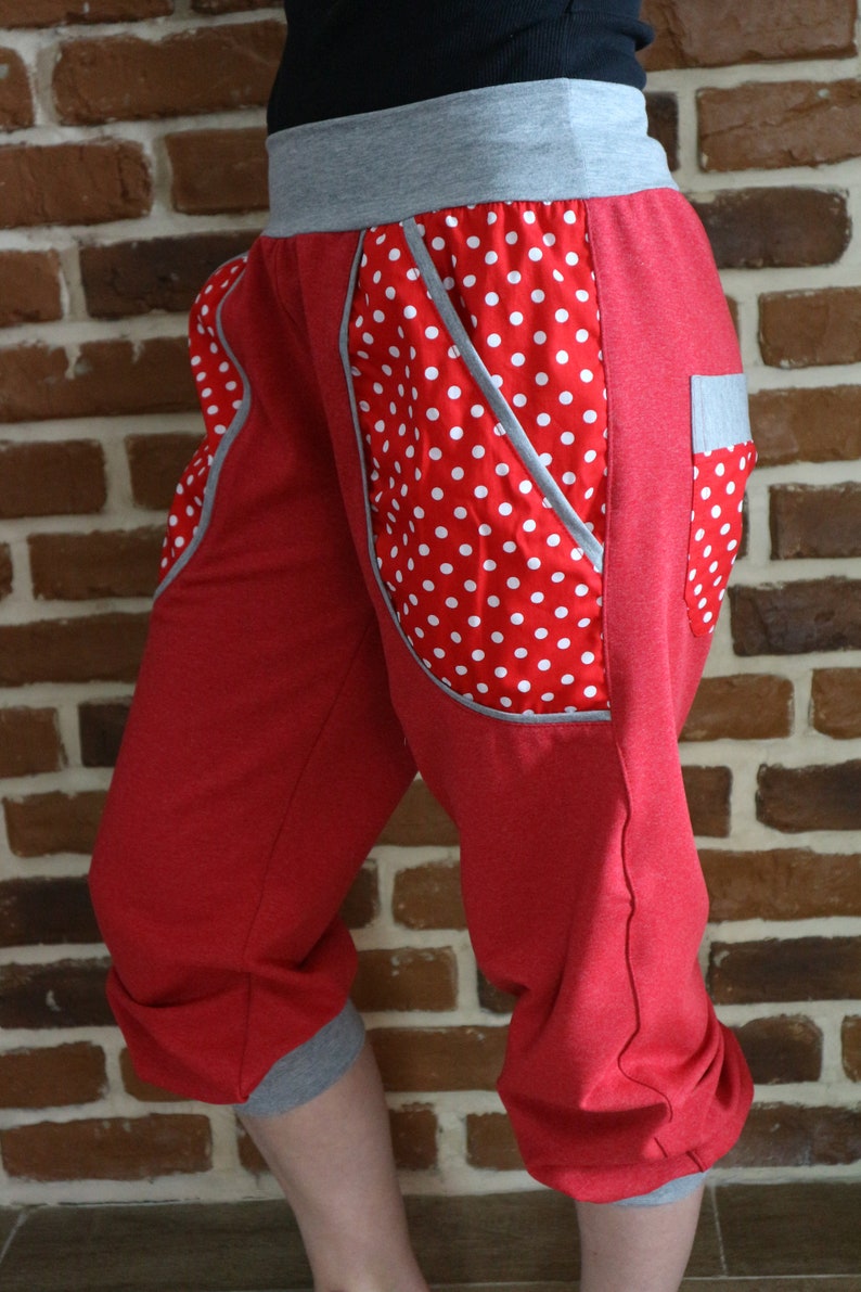 May include: Red capri pants with white polka dots and gray trim. The pants have a unique design with a large pocket on the side.