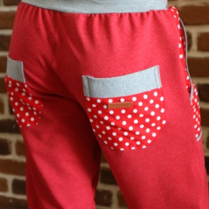 May include: Red sweatpants with a grey waistband and two pockets. The pockets have a white polka dot fabric lining.