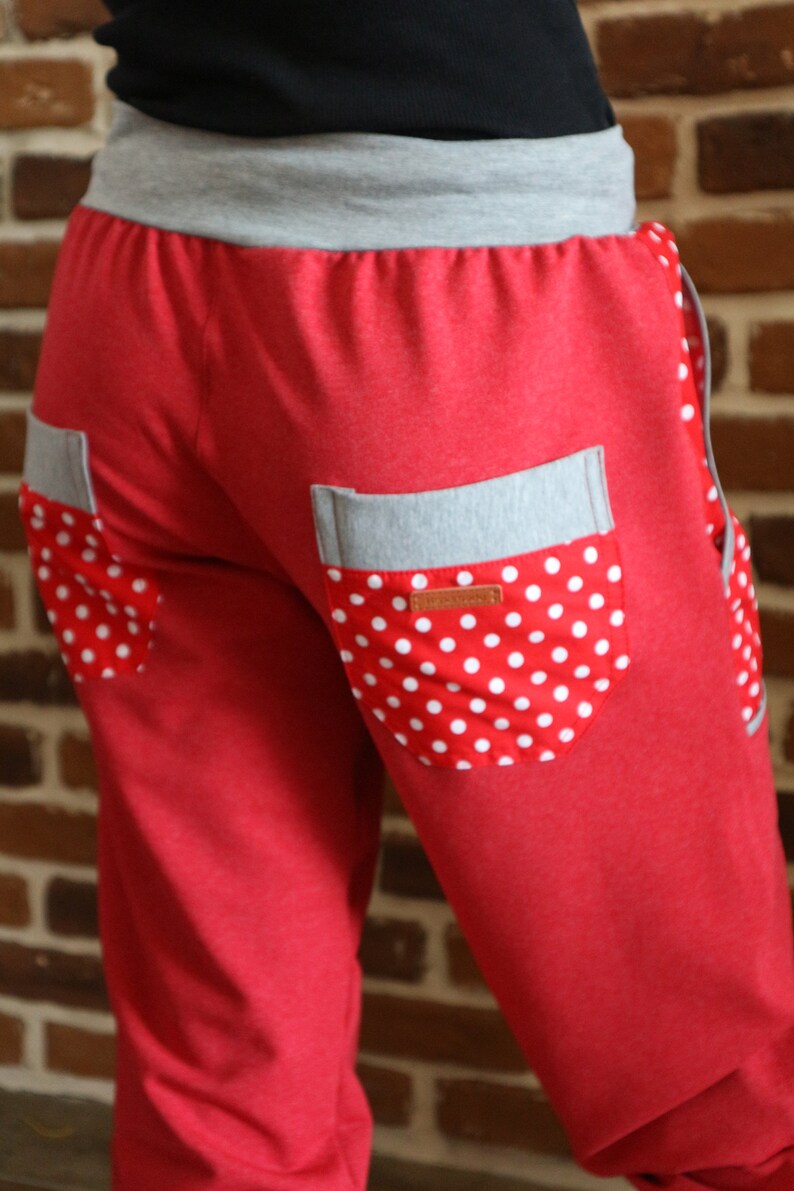 May include: Red sweatpants with a grey waistband and two pockets. The pockets have a white polka dot fabric lining.