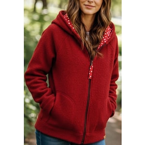 May include: A red hooded zip-up jacket with a textured exterior. The interior of the hood features a white fabric with red polka dots. The jacket has a black zip and two front pockets. The zip pull has a matching polka dot design.