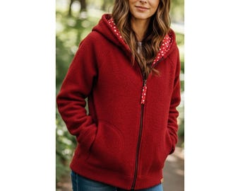 May include: A red hooded zip-up jacket with a textured exterior. The interior of the hood features a white fabric with red polka dots. The jacket has a black zipper and two front pockets. The zipper pull has a matching polka dot design.