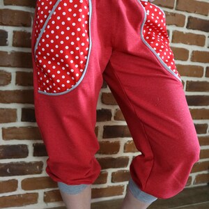 May include: Red sweatpants with grey waistband and cuffs. The sweatpants have large pockets on the sides with white polka dots on a red background.