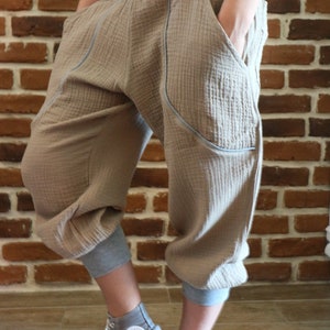May include: A pair of beige, loose-fitting pants with a gray waistband and contrasting stitching. The pants have pockets on the sides and are cuffed at the ankles. The person is wearing gray high-top sneakers.