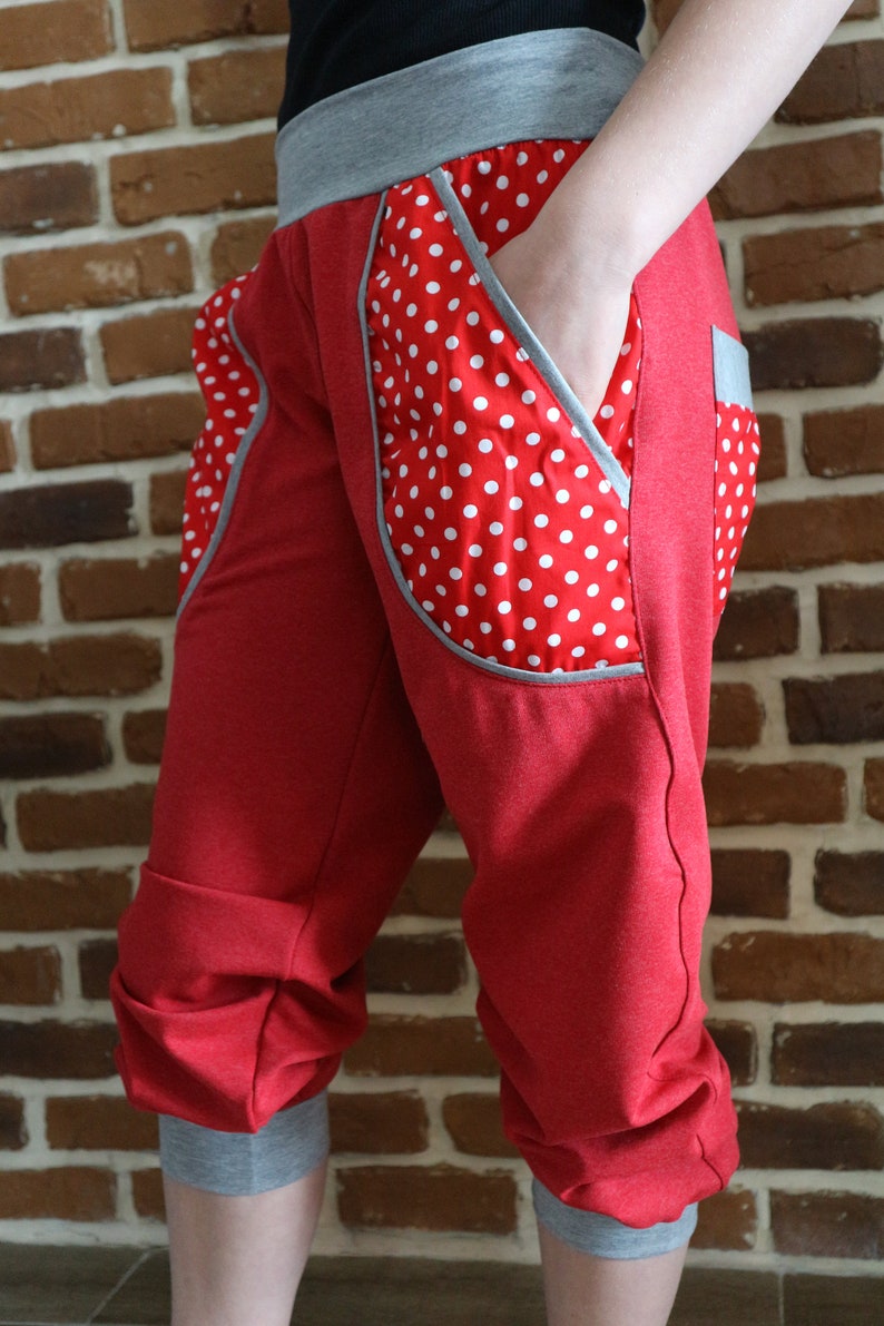 May include: Red capri pants with a white polka dot fabric detail on the side pockets. The pants have a gray waistband and cuffs.
