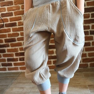May include: Beige cotton pants with a gray waistband and cuffed legs. The pants have large pockets on the sides and a textured fabric. The person is wearing gray sneakers.