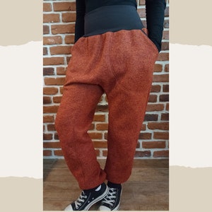 May include: A pair of rust-coloured, loose-fitting trousers with a wide waistband and large pockets. The trousers are made of a soft, textured fabric.
