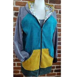 Könnte beinhalten: Ein türkisfarbener, grauer und gelber Cord-Hoodie mit Reißverschluss. Der Hoodie hat eine Kapuze mit einem Blumenfutter.