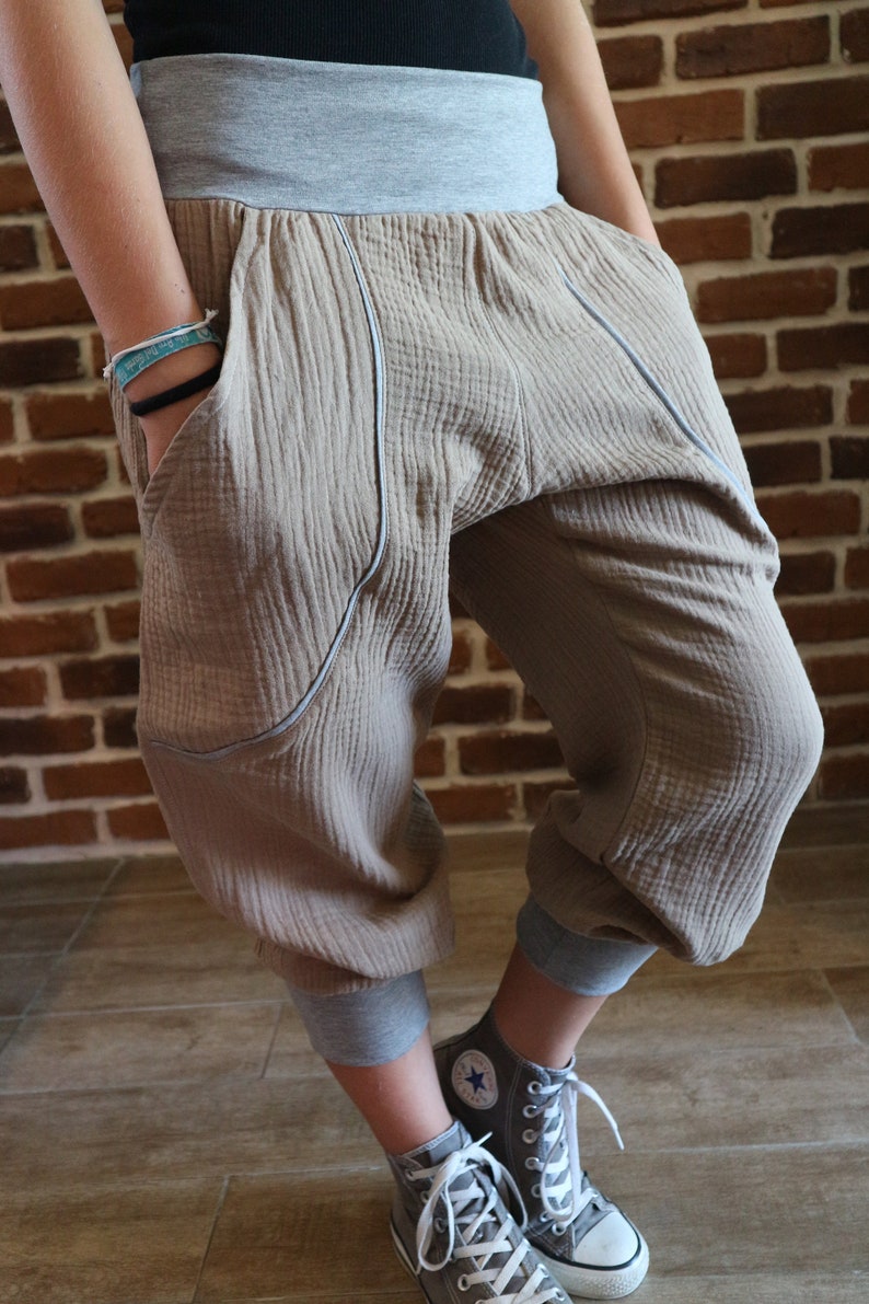 May include: Beige cotton pants with a gray waistband and gray cuffs. The pants have a loose, baggy fit and are styled with gray high-top sneakers.