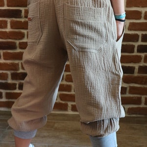 May include: Beige cotton pants with a grey elastic waistband and cuffed legs. The pants have two large pockets in the back.