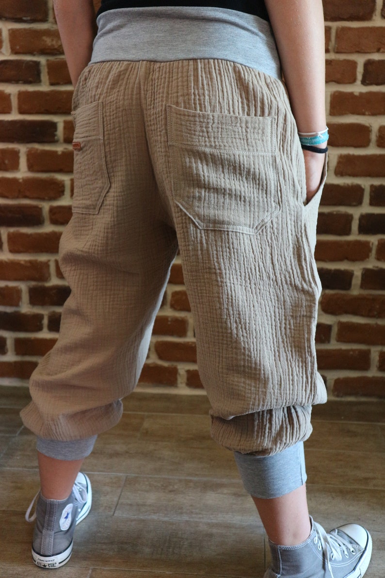May include: Beige cotton pants with a grey elastic waistband and cuffed legs. The pants have two large pockets in the back.